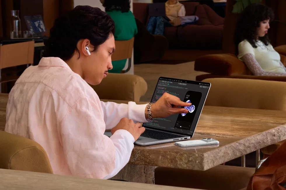 En bruger sidder ved et bord og rører ved skærmen på sin MacBook Pro med PROLED XDR-skærm.